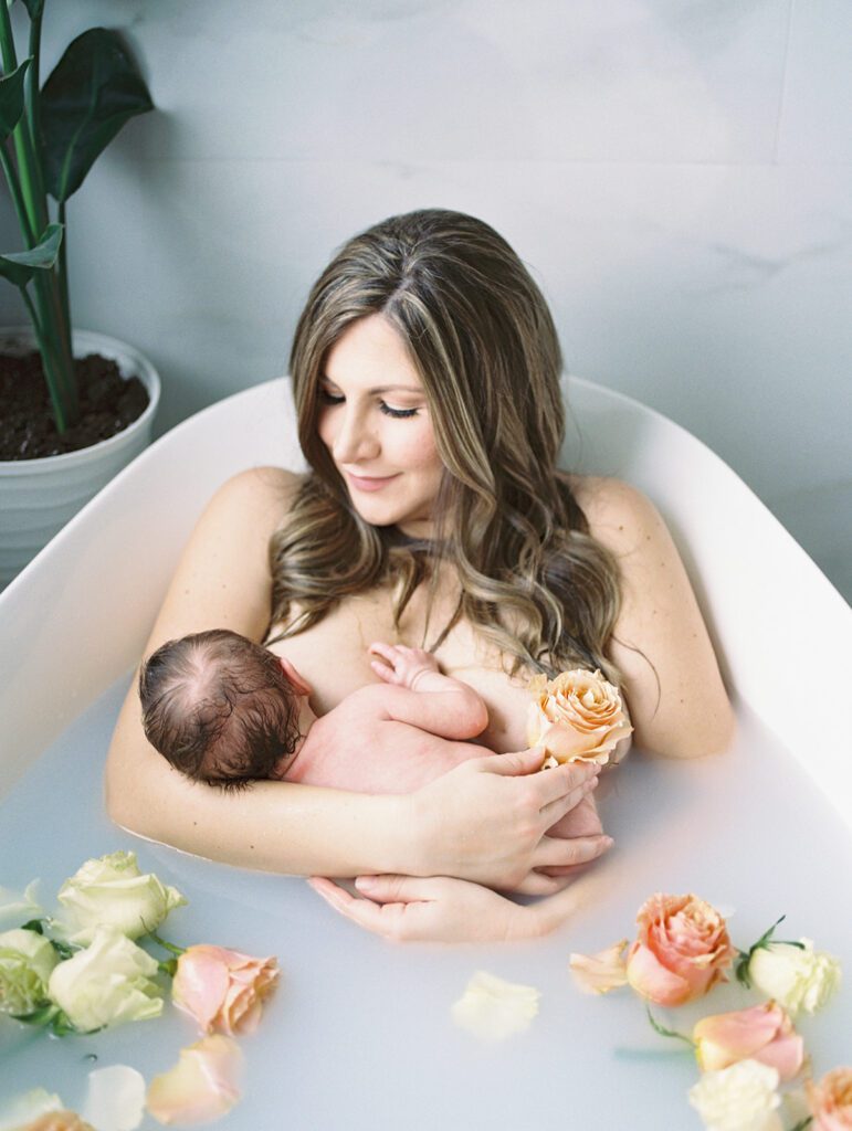 Mother smiles while holding her newborn daughter during a milk bath photoshoot.