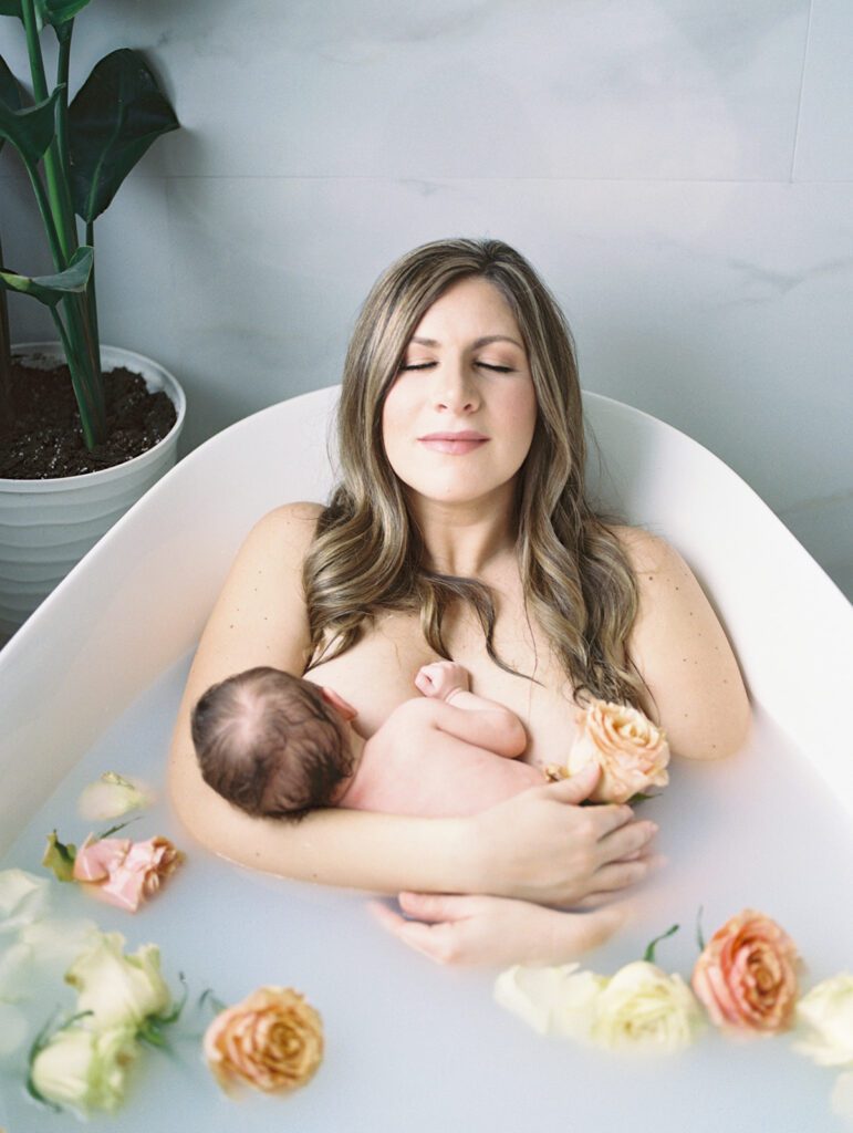 Mother closes her eyes and slightly lifts her head as she holds her newborn baby in a milk bath during their newborn session.