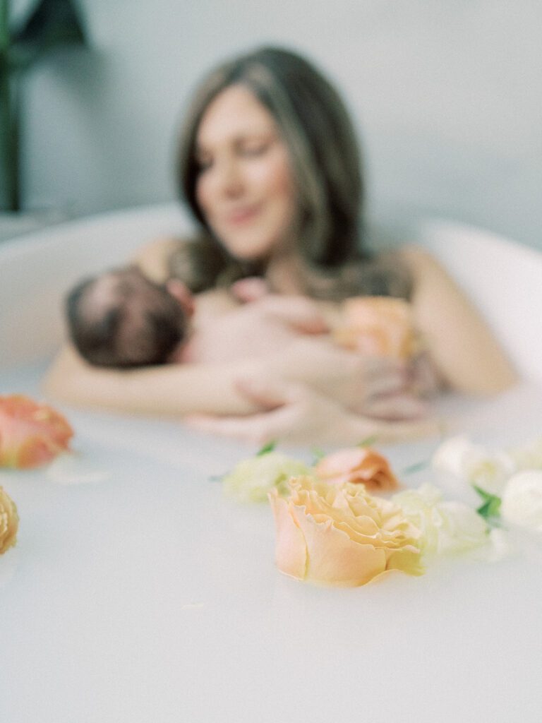 Close up view of an orange rose in a milk bath while a mother nurses her baby in the background.