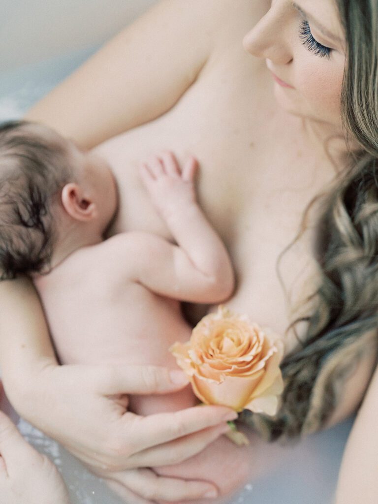 Naked mother holds her newborn baby girl up to her chest as baby nurses.
