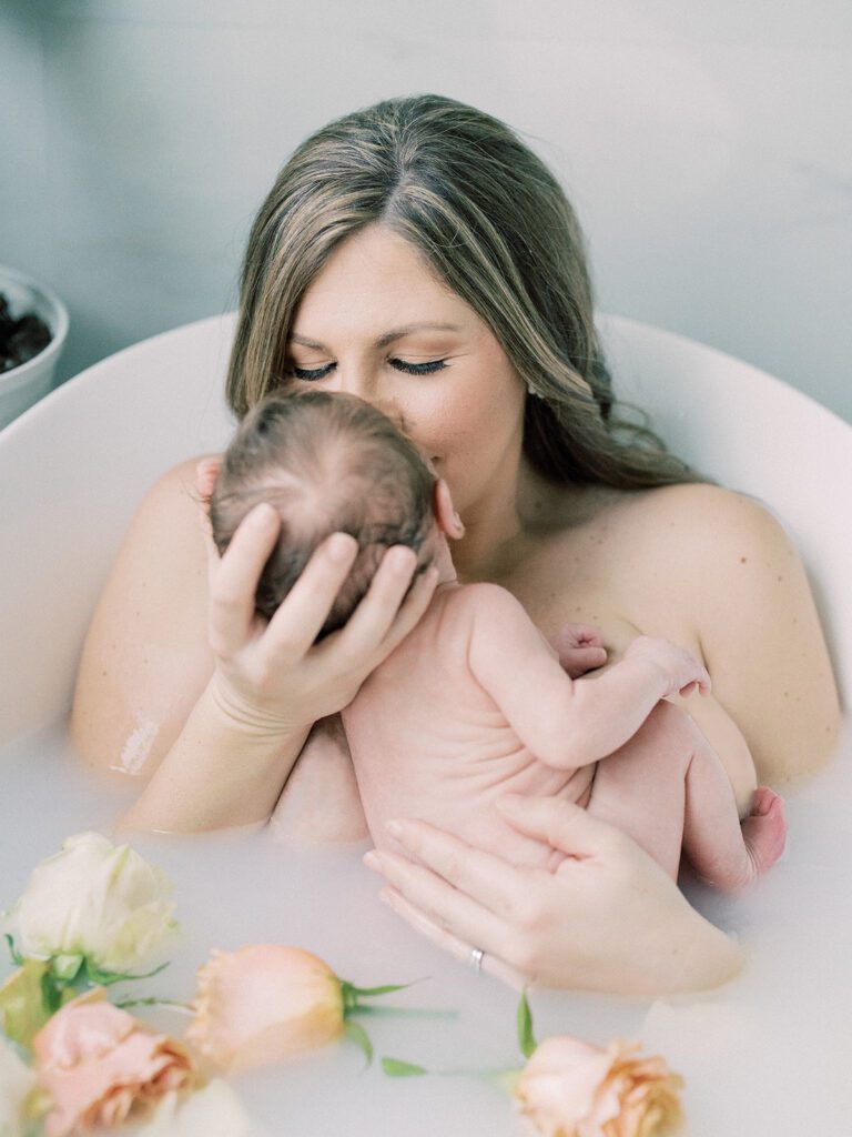 Milk bath photoshoots of a mother holding her newborn daughter up to her face in a tub with florals.