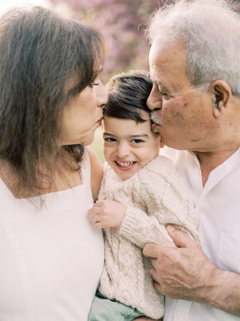 A grandmother and grandfather lean in to kiss their grandson.