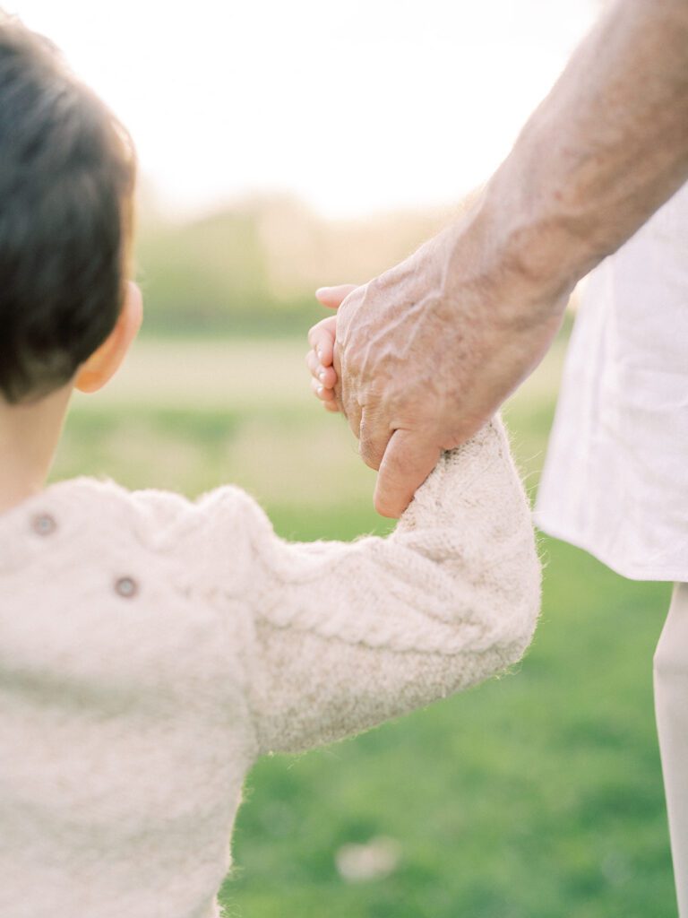 A close-up view of a little boy holding his grandfather's hand.