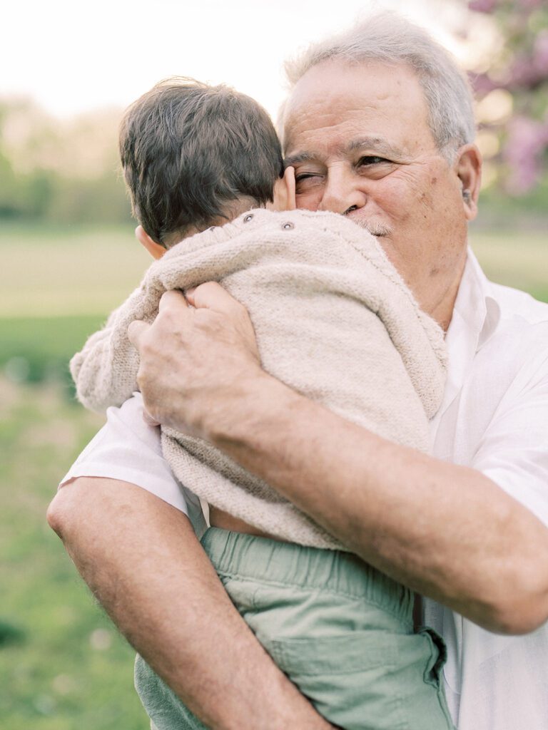 A grandfather holds his young grandson in his arms and smiles.