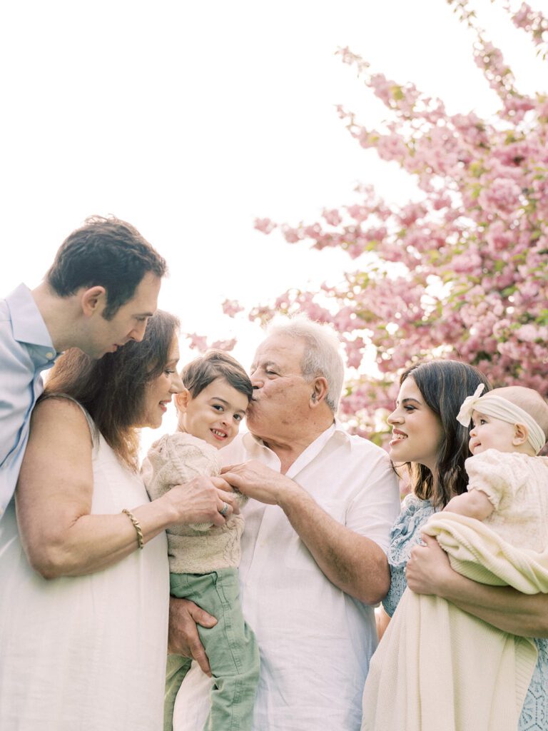 A family of six leans in together underneath a pink cherry tree.