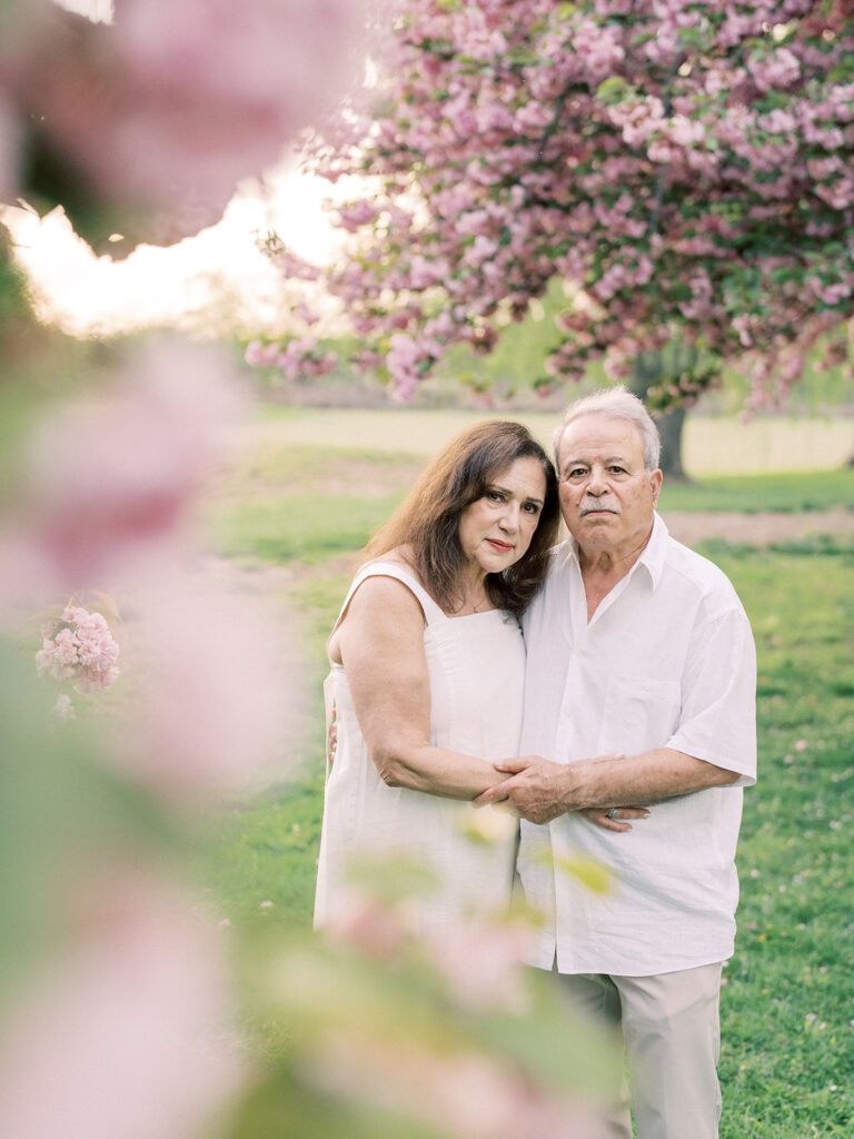 An older woman and man stand together among pink cherry trees in DC.