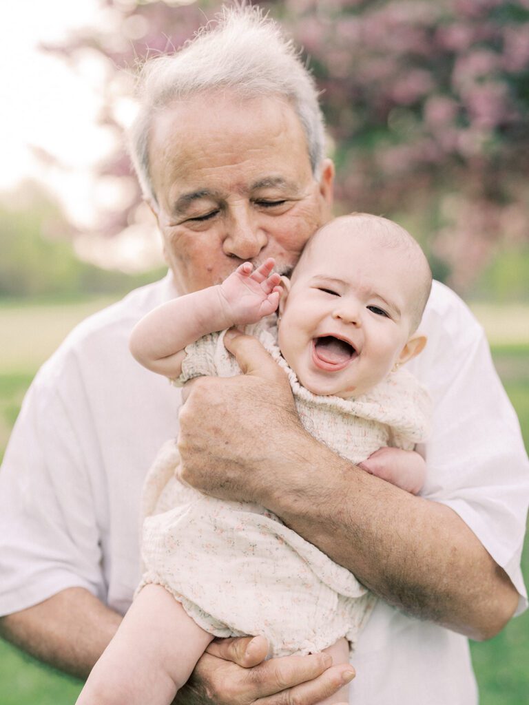 A grandfather holds his granddaughter up to give her a kiss on her cheek.